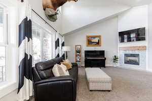 Living area with a fireplace, baseboards, carpet floors, and high vaulted ceiling