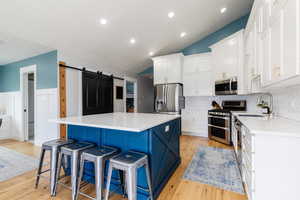 Kitchen with decorative backsplash, appliances with stainless steel finishes, a kitchen breakfast bar, and white cabinets