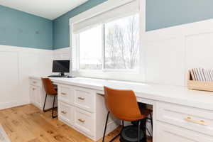 Office space featuring wainscoting, built in desk, light wood-type flooring, and a decorative wall