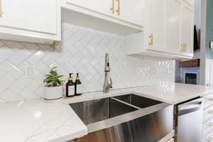 Kitchen with light stone counters, tasteful backsplash, a sink, a fireplace, and white cabinets