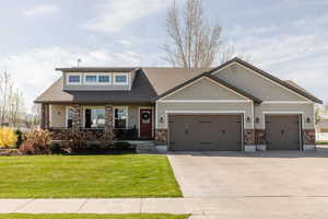 Craftsman-style house featuring stone siding, a porch, a front lawn, and a garage