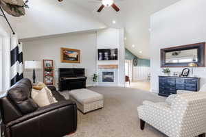 Living area with a wainscoted wall, carpet, ceiling fan, a tile fireplace, and high vaulted ceiling