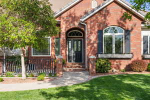 View of exterior entry with brick siding, fence, and a yard