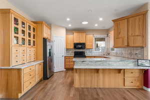 Kitchen featuring tasteful backsplash, black appliances, glass insert cabinets, light wood-type flooring, and a peninsula