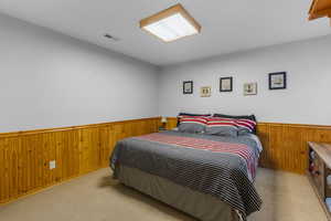 Carpeted bedroom with visible vents, a wainscoted wall, and wood walls