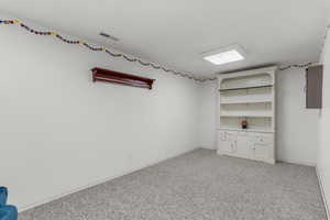 Interior space featuring electric panel, baseboards, visible vents, and light colored carpet