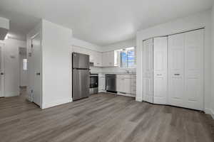 Kitchen with light countertops, light wood-style floors, baseboards, appliances with stainless steel finishes, and white cabinetry