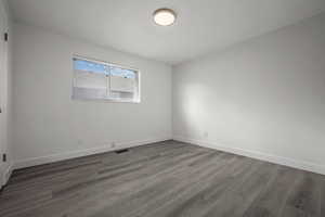 Empty room featuring visible vents, baseboards, and dark wood-style floors