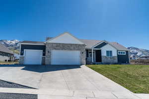 Ranch-style home featuring a mountain view, stone siding, a front yard, and a garage