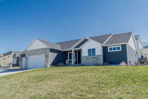 Single story home featuring a front lawn, driveway, stone siding, and a garage