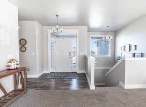 Foyer entrance featuring wood finished floors, carpet floors, baseboards, and an inviting chandelier