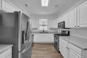 Kitchen with laminate floors, white cabinets, and stainless steel appliances