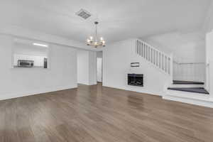 Unfurnished living room with a chandelier, laminate floors, fireplace, and stairway