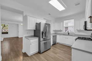Kitchen with laminate floors, white cabinets, and stainless steel appliances