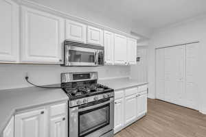 Kitchen with laminate floors, white cabinets, and stainless steel appliances