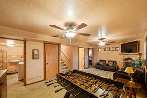Carpeted living area with a textured ceiling, visible vents, a ceiling fan, a brick fireplace, and stairs