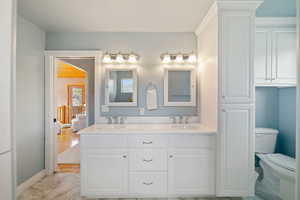Bathroom featuring marble finish floor, double vanity, toilet, and a sink