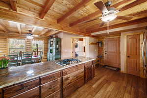 Kitchen with wooden ceiling, stacked washing maching and dryer, stainless steel gas cooktop, log walls, and ceiling fan