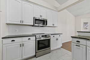 Kitchen featuring white cabinets, stainless steel appliances, vaulted ceiling, and marble finish floor