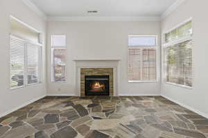 Unfurnished living room featuring stone floors, visible vents, crown molding, and plenty of natural light