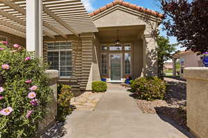 Doorway to property featuring a tile roof, a pergola, and stucco siding