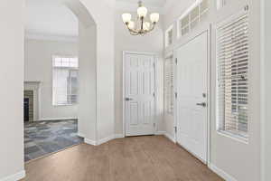Entrance foyer with light wood-style flooring, arched walkways, baseboards, a chandelier, and ornamental molding