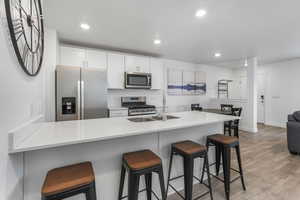 Kitchen with a breakfast bar area, stainless steel appliances, light wood finished floors, and a sink