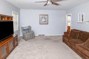Living area featuring ceiling fan, light carpet, visible vents, and a wealth of natural light