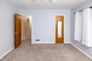 Carpeted empty room with visible vents, a ceiling fan, and baseboards