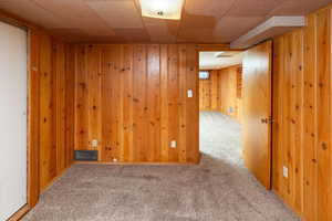 Unfurnished room with wooden walls, visible vents, and carpet