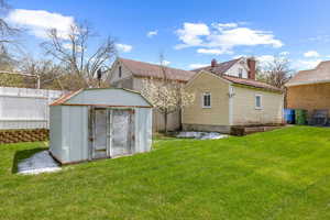 Back of house featuring a lawn, an outdoor structure, a storage shed, and cooling unit