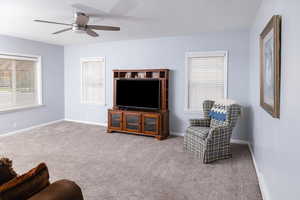 Carpeted living room with ceiling fan, a wealth of natural light, and visible vents