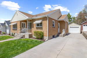 Bungalow-style house with an outbuilding, concrete driveway, a garage, brick siding, and a front yard