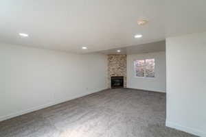 Unfurnished living room featuring a textured ceiling, a glass covered fireplace, carpet, and recessed lighting