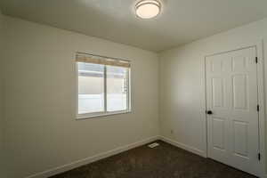 Unfurnished room featuring baseboards, dark colored carpet, and visible vents