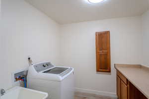 Laundry area with a sink, light wood-type flooring, cabinet space, baseboards, and washer / clothes dryer