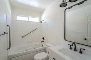 Full bath with toilet, vanity, a textured ceiling, and a combined bath / shower with jetted tub