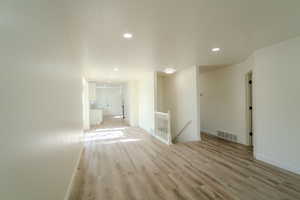 Interior space featuring light wood-type flooring, baseboards, visible vents, and an upstairs landing