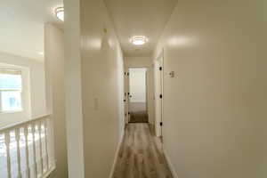 Corridor featuring light wood-style floors, a textured ceiling, and baseboards