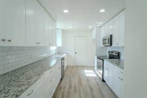 Kitchen featuring decorative backsplash, light stone counters, stainless steel appliances, and a sink