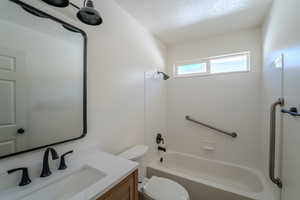 Bathroom featuring toilet, shower / bathtub combination, vanity, and a textured ceiling