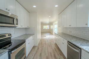 Kitchen with light wood-style floors, appliances with stainless steel finishes, and white cabinetry