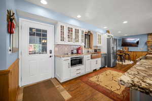 Kitchen featuring a sink, stainless steel appliances, white cabinetry, light stone countertops, and dark wood-type flooring