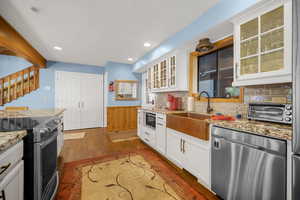 Kitchen with light stone counters, a sink, appliances with stainless steel finishes, backsplash, and dark wood-style flooring