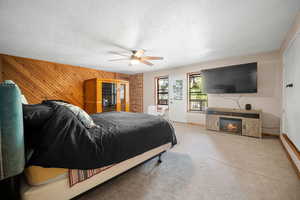 Carpeted bedroom featuring ceiling fan, wood walls, a lit fireplace, and baseboards
