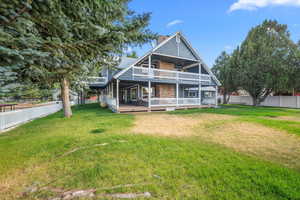 Back of house featuring a wooden deck, a yard, a chimney, and fence