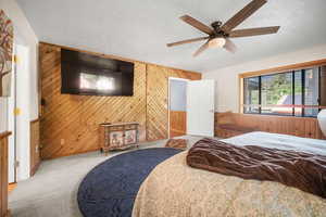 Bedroom with carpet, a textured ceiling, wood walls, and a ceiling fan