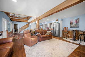 Living room with a wealth of natural light, dark wood-style flooring, stairs, and beam ceiling