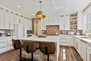 Kitchen featuring a breakfast bar, a sink, appliances with stainless steel finishes, custom exhaust hood, and dark wood-style flooring