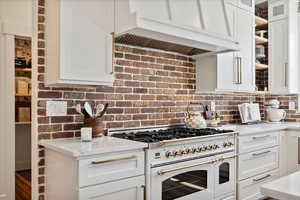 Kitchen featuring glass insert cabinets, range with two ovens, white cabinetry, and custom range hood